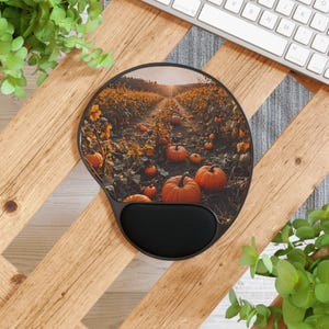 May include: Ergonomic mouse pad with a wrist rest. The pad features a fall scene with pumpkins in a field, a dirt path, and a sunset. The pad is black with a black wrist rest.