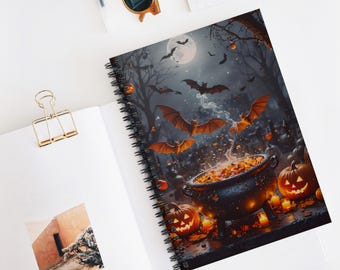 May include: A spiral-bound notebook with a Halloween-themed cover. The cover features a spooky scene with bats, a full moon, jack-o'-lanterns, and a cauldron. The notebook is open on a white surface with a gold paper clip.