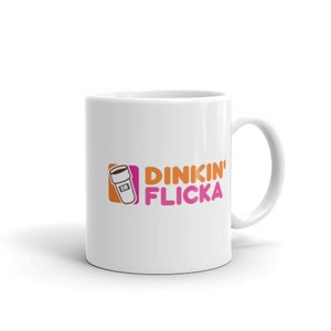 May include: White ceramic mug featuring a pink and orange logo that reads "DINKIN' FLICKA" and a stylised image of a coffee cup.