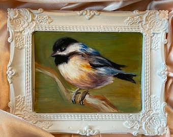 Puede incluir: Una pintura al óleo enmarcada de un pequeño pájaro con plumas negras, blancas, azules y marrones posado en una rama. El pájaro está pintado en un estilo realista con detalles visibles como su pico y ojos. El marco es blanco con detalles ornamentados.