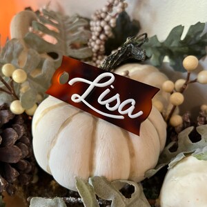 May include: A white faux pumpkin with a brown and black tortoiseshell name tag that says "Lisa" in white script.