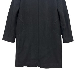 Peut inclure: Un manteau noir au design classique. Le manteau pr&eacute;sente une coupe mi-longue, des manches trois-quarts et deux poches arrondies. Le manteau est fait d'une mati&egrave;re noire &eacute;paisse et unie.
