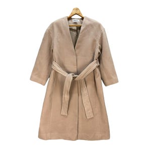 May include: A beige, knee-length coat with a wrap-around belt. The coat has a V-neck and three-quarter sleeves. The coat is hanging on a wooden hanger. The brand name "SNIDEL" is visible on the label.