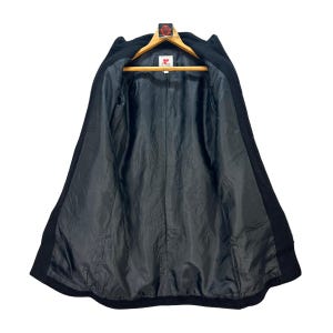 Peut inclure: Manteau en laine noir suspendu &agrave; un cintre en bois. Le manteau est ouvert, r&eacute;v&eacute;lant une doublure noire. Le manteau a un design classique avec un col crant&eacute; et une coupe ajust&eacute;e. C'est un article vintage.
