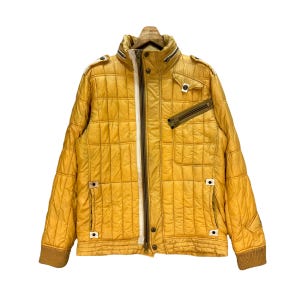 May include: Mustard yellow quilted jacket with a high collar and multiple pockets. The jacket features a full-length zipper with a white stripe down the center and brown ribbed cuffs. The jacket is hanging on a wooden hanger.