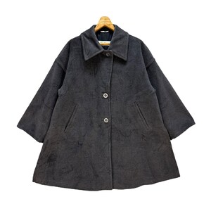 May include: A dark gray coat with a wide collar and three buttons. The coat has two front pockets and short sleeves. The coat is hanging on a wooden hanger.