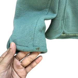 May include: A teal green jacket with a long sleeve. The sleeve has a seam down the center and a fold at the bottom.