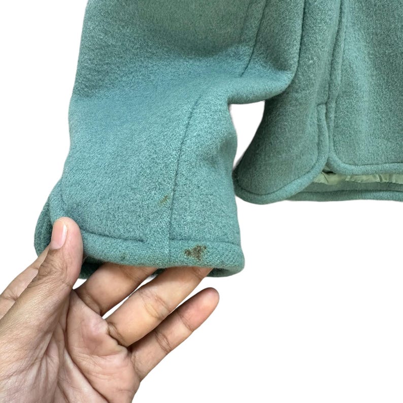 May include: A teal green jacket with a long sleeve. The sleeve has a seam down the center and a fold at the bottom.