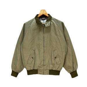 Könnte beinhalten: Eine hellbraune Bomberjacke mit Reißverschluss und grünem Kragen. Die Jacke hat zwei Taschen auf der Vorderseite und einen gerippten Saum und Bündchen.