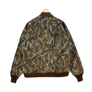 May include: A camouflage bomber jacket with a brown collar, cuffs, and hem. The jacket features a tree bark pattern in shades of brown, green, and tan. The back of the jacket is visible, showcasing the full design.