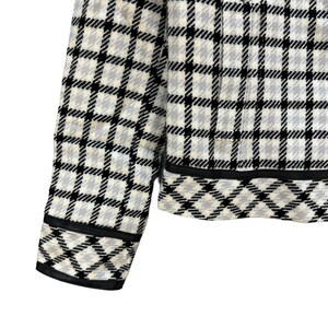 May include: A white and black checked jacket with a black trim. The jacket has a zip fastening and long sleeves.