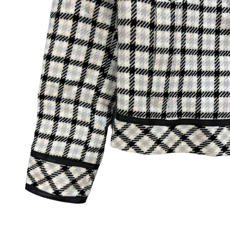 May include: A white and black checked jacket with a black trim. The jacket has a zip fastening and long sleeves.
