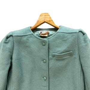May include: A light blue wool blazer with a button closure and a single pocket. The label reads "Courr&egrave;ges Paris Est. 1961".