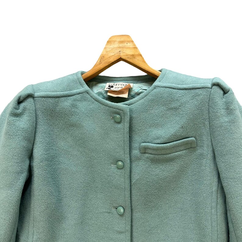 May include: A light blue wool blazer with a button closure and a single pocket. The label reads "Courr&egrave;ges Paris Est. 1961".