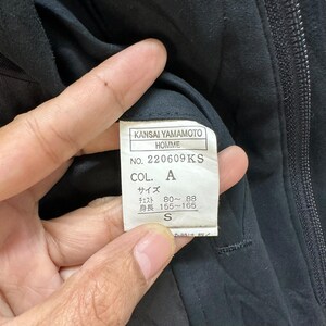 Może przedstawiać: Czarna metka odzieżowa z białym tekstem, na kt&oacute;rej widnieje napis "KANSAI YAMAMOTO HOMME NO. 220609KS COL. A サイズ チェスト 80~88 身長 155~165 S"