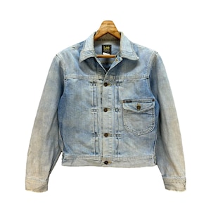 May include: Pale blue denim jacket with a classic collar, button-down front, and a chest pocket. The jacket has a faded wash and is labelled "Lee". The jacket is displayed on a wooden hanger.