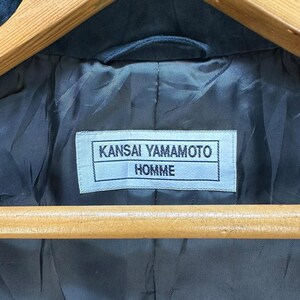 Może przedstawiać: Czarna kurtka z białą metką z napisem "Kansai Yamamoto Homme".