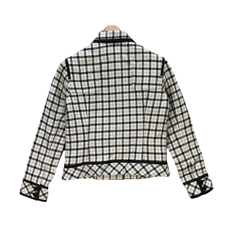 May include: A white and black checked blazer with a black trim around the collar, cuffs, and hem. The blazer has a fitted silhouette and a button closure.