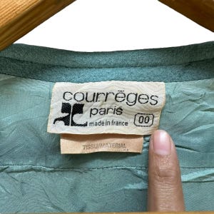 May include: A light blue label with the text "Courr&egrave;ges Paris made in France 00" in black. The label is attached to a light blue fabric.