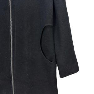 Peut inclure: Un manteau noir avec une fermeture &eacute;clair pleine longueur et une grande poche incurv&eacute;e. Le manteau a un design simple et minimaliste et un aspect l&eacute;g&egrave;rement textur&eacute;. La manche est visible sur le c&ocirc;t&eacute; droit.
