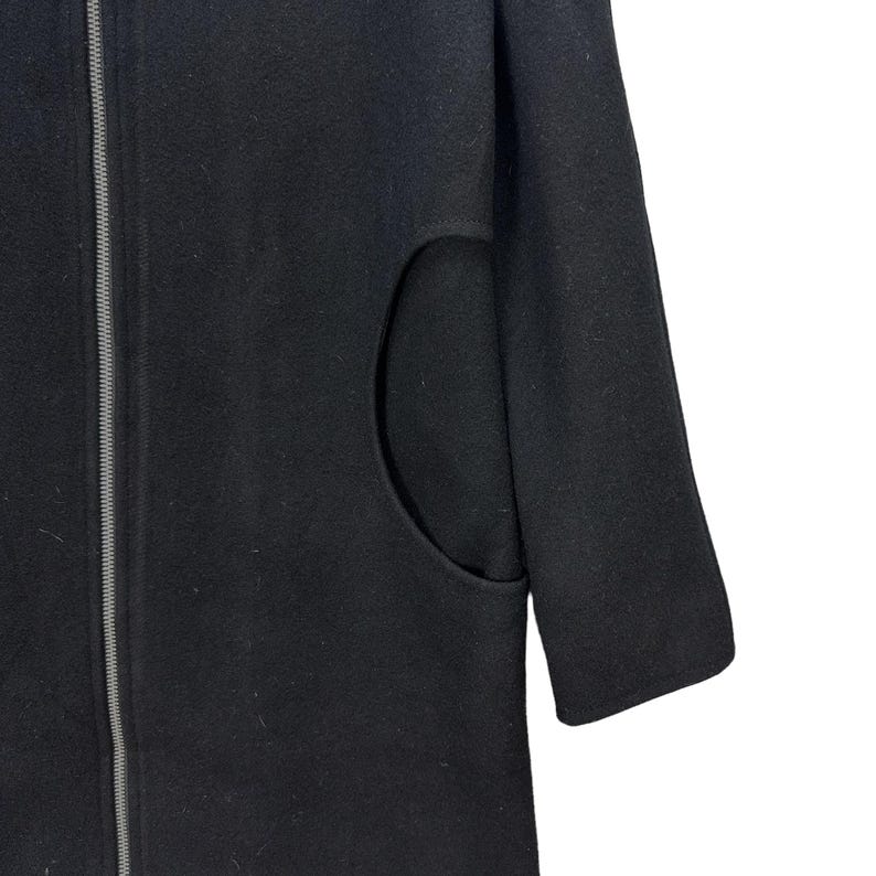Peut inclure: Un manteau noir avec une fermeture &eacute;clair pleine longueur et une grande poche incurv&eacute;e. Le manteau a un design simple et minimaliste et un aspect l&eacute;g&egrave;rement textur&eacute;. La manche est visible sur le c&ocirc;t&eacute; droit.