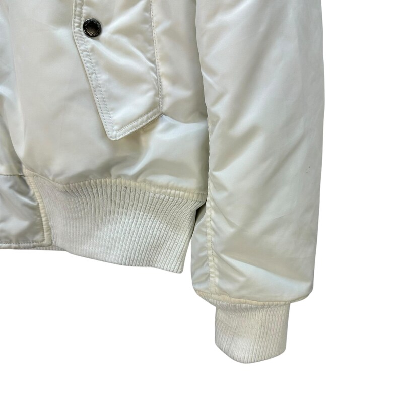 Pu&ograve; includere: Giacca bomber color crema con polsini e orlo a coste. La giacca presenta una tasca frontale e una chiusura con bottoni. La manica ha un polsino a coste. La giacca &egrave; realizzata in un materiale liscio, possibilmente nylon o poliestere.