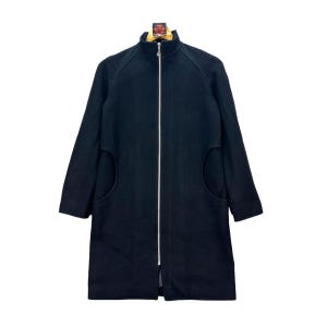 Peut inclure: Un manteau en laine noir avec un col montant et une fermeture &eacute;clair sur toute la longueur. Le manteau a deux grandes poches arrondies et des manches longues. Le manteau est de couleur noire unie et est pr&eacute;sent&eacute; sur fond blanc.
