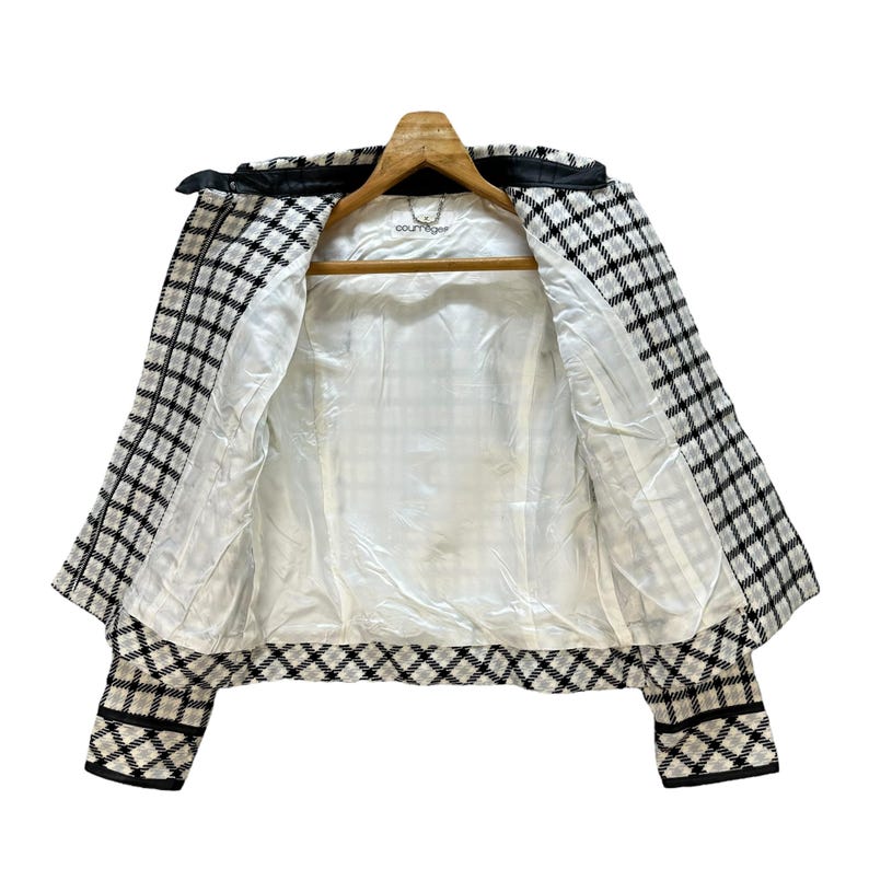 May include: A black and white plaid jacket with a diamond pattern on the bottom. The jacket has a white lining and a label that says "Couture" on the inside.