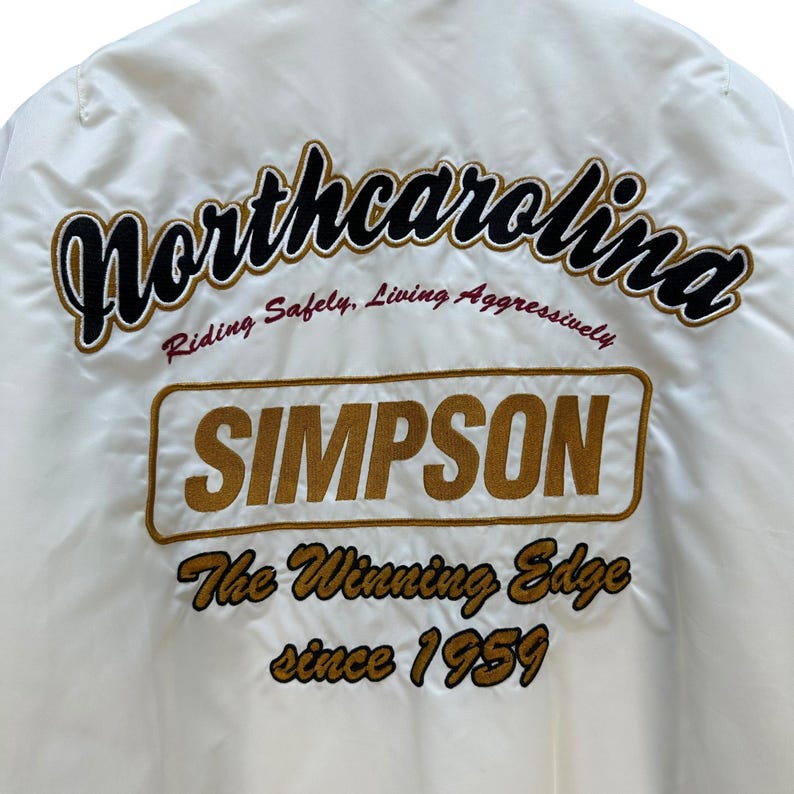 Pu&ograve; includere: Giacca color crema con scritte ricamate. La parola "Northcarolina" &egrave; arcuata nella parte superiore in corsivo nero e oro. Sotto c'&egrave; "SIMPSON" in un rettangolo dorato. Il testo "The Winning Edge since 1959" &egrave; sotto.