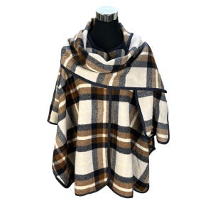 May include: A white, brown, and navy blue plaid poncho with a navy blue trim. The poncho is folded and draped over a mannequin.
