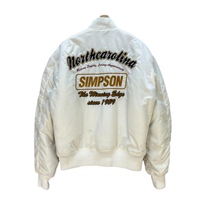Pu&ograve; includere: Giacca bomber color crema con polsini e orlo a coste. Il retro presenta un testo ricamato in marrone e oro, tra cui "Northcarolina", "SIMPSON" e "The Winning Edge since 1959."