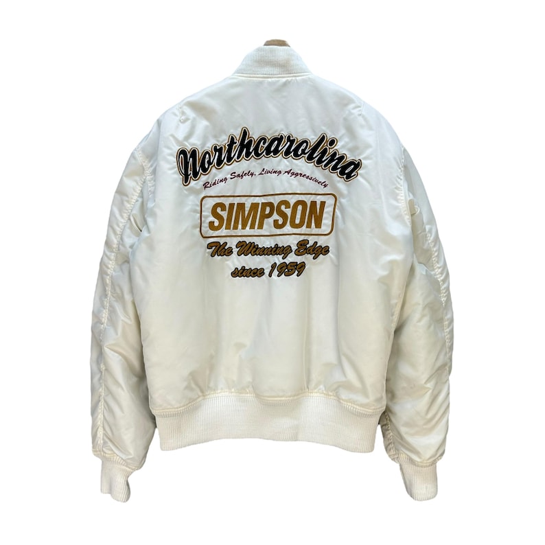 Pu&ograve; includere: Giacca bomber color crema con polsini e orlo a coste. Il retro presenta un testo ricamato in marrone e oro, tra cui "Northcarolina", "SIMPSON" e "The Winning Edge since 1959."