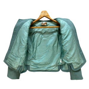 May include: A teal blue cropped jacket with a satin lining. The jacket has a button closure and long sleeves.