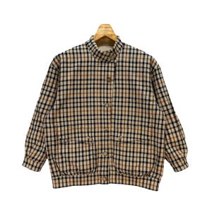 May include: A vintage jacket with a brown, black, and beige plaid pattern. The jacket has a high collar, button-up front, and two front pockets. The jacket is hanging on a wooden hanger.