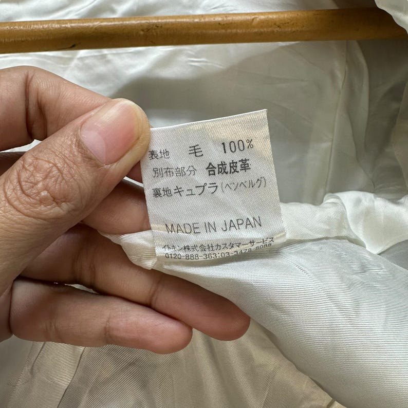 May include: A white fabric label with black text that reads "表地 毛 100% 別布部分 合成皮革 裏地 キュプラ(ベンベルグ) MADE IN JAPAN イトキン株式会社カスタマーサービス 0120-888-363:03-3478-808"