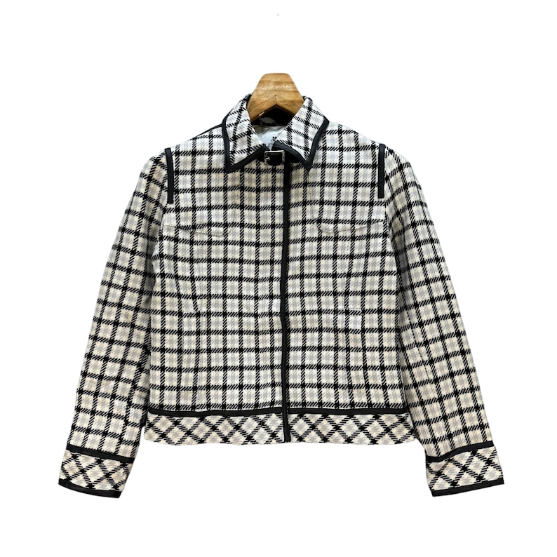 May include: A black and white checked jacket with a black zip and black trim. The jacket has a collar and long sleeves.