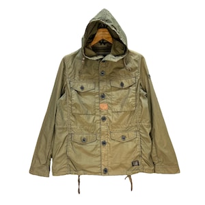 Może przedstawiać: Zielona kurtka z kapturem w kolorze oliwkowym z wieloma przednimi kieszeniami i zapięciami na guziki. Kurtka posiada kaptur i dół ze sznurkiem oraz małą naszywkę na piersi. Kurtka ma styl vintage i użytkowy.