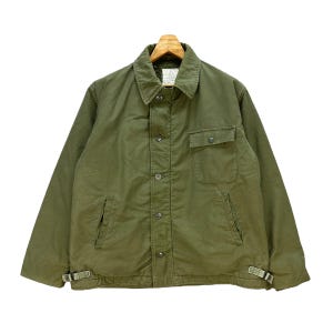 May include: Olive green jacket with a button-up front, two chest pockets, and two side pockets. The jacket has a collar and adjustable straps at the waist. The jacket is hanging on a wooden hanger.