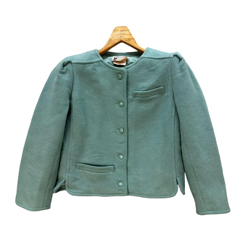 May include: A light blue blazer with a button-up front and two pockets. The blazer has a slightly puffed shoulder design.