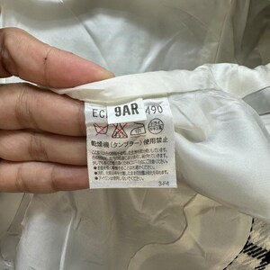 May include: A white fabric label with black text that reads "EC 9AR 490". The label has a red and white symbol with a diagonal line through it. The text below the symbol reads "乾燥機(タンブラー)使用禁止" in Japanese. The text below that reads "This fabric is delicate and may be damaged by washing or drying. Please handle with care. Do not use a tumble dryer. Do not iron. Do not bleach. Do not dry clean. 3-F4" in English.