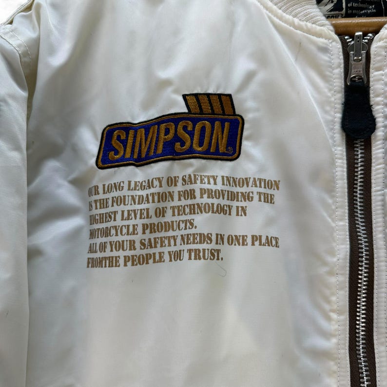 Pu&ograve; includere: Giacca da moto color crema con chiusura a zip e toppa "SIMPSON". La toppa &egrave; blu con scritte dorate e bordo dorato. La giacca riporta la scritta "OUR LONG LEGACY OF SAFETY INNOVATION..." e "ALL OF YOUR SAFETY NEEDS IN ONE PLACE."