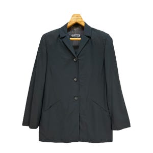 Peut inclure: Un blazer gris foncé à fermeture simple et quatre boutons. Le blazer a un col et deux poches. L'étiquette "Jil Sander" est visible à l'intérieur du col.