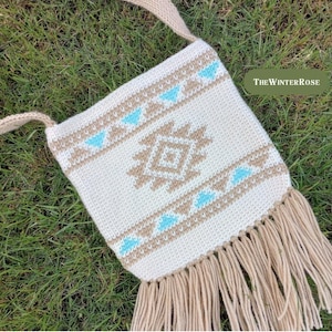 Könnte beinhalten: Cremefarbene gehäkelte Umhängetasche mit einem geometrischen Muster in Beige und Türkis. Die Tasche hat einen langen Riemen und Fransen am unteren Rand. Der Text "The Winter Rose" ist auf der rechten Seite der Tasche zu sehen.