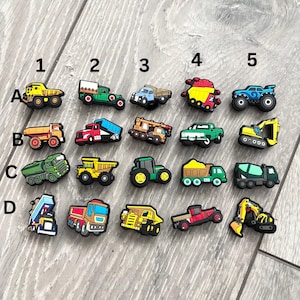 Pode incluir: Uma coleção de amuletos coloridos em miniatura de veículos de construção. O conjunto inclui vários caminhões, tratores e escavadeiras em tons de amarelo, verde, vermelho e azul. Estes amuletos são provavelmente projetados para fins decorativos, como acessórios para sapatos.
