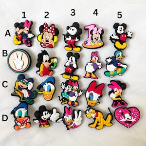 Peut inclure: Une collection de breloques de personnages de dessins animés colorés, dont Mickey Mouse, Minnie Mouse, Donald Duck et Daisy Duck. Les breloques présentent diverses poses et designs, avec des couleurs vives et des détails. Ces breloques sont probablement pour chaussures ou accessoires.