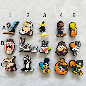 May include: A set of 15 colourful cartoon character shoe charms featuring characters from the Looney Tunes franchise, including Bugs Bunny, Tweety Bird, Daffy Duck, Road Runner, and Tasmanian Devil.