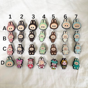 May include: A set of 24 colourful bunny charms with different designs and colours. The charms are arranged in a grid pattern with letters A through D and numbers 1 through 7 labelling the rows and columns. The charms are made of a soft, rubbery material and are perfect for adding a touch of whimsy to any project.