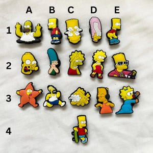 Puede incluir: Una colección de dijes de zapatos de personajes de dibujos animados en varias poses y atuendos. Los dijes presentan personajes con piel amarilla, que usan diferentes ropas y accesorios. Los dijes están diseñados para ser adheridos a los zapatos.