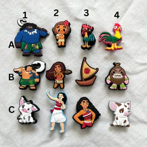 Könnte beinhalten: Set mit 12 Moana-Schuhcharms mit Charakteren wie Maui, Moana, Pua, Hei Hei und mehr. Die Charms sind aus buntem Gummi und perfekt, um deinen Schuhen einen Hauch von Disney-Magie zu verleihen.