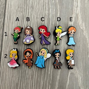 May include: A set of ten colourful cartoon character shoe charms featuring characters like Peter Pan, Ariel, Cinderella, and Tinkerbell. The charms are arranged in two rows of five, labelled A through E and 1 through 2.